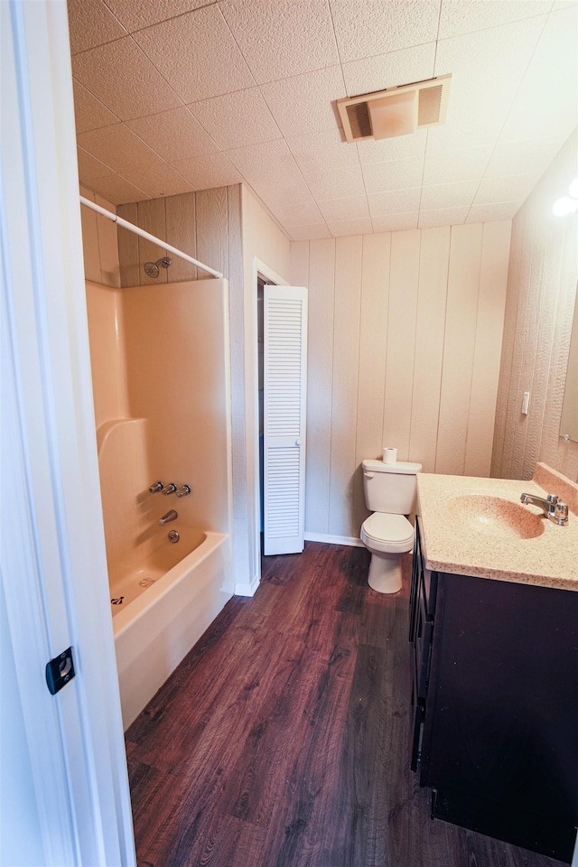 full bathroom featuring toilet, wood-type flooring, vanity, wooden walls, and shower / washtub combination