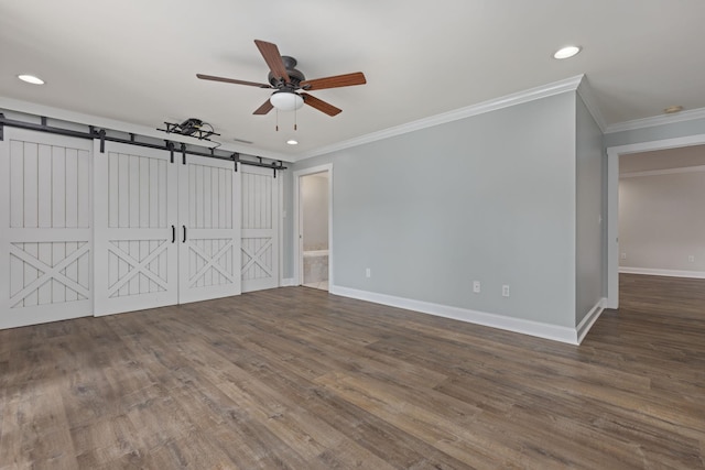 empty room featuring crown molding, dark wood finished floors, baseboards, and a barn door