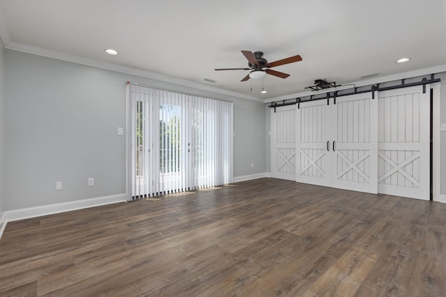 empty room with dark wood-style floors, a barn door, ornamental molding, a ceiling fan, and baseboards