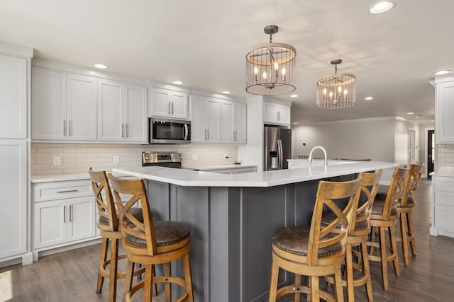 kitchen with stainless steel appliances, a large island with sink, light countertops, and hanging light fixtures