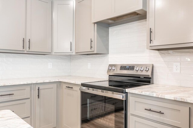 kitchen featuring stainless steel electric range, tasteful backsplash, wood-type flooring, light stone countertops, and custom exhaust hood