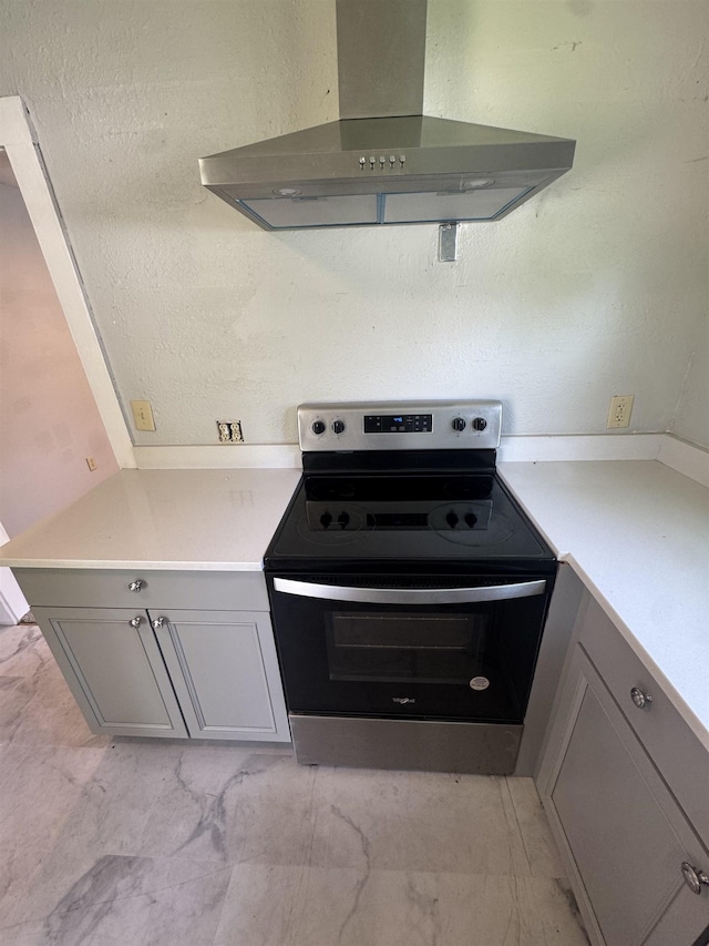  - kitchen with ventilation hood, stainless steel electric stove, gray cabinetry, and light marble finish flooring