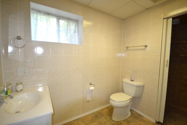 bathroom featuring a paneled ceiling, tile patterned flooring, tile walls, and toilet