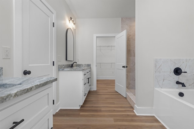 full bath featuring a tile shower, a spacious closet, wood finished floors, vanity, and a bath