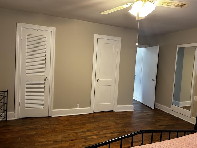 unfurnished bedroom featuring two closets, dark hardwood / wood-style floors, and ceiling fan