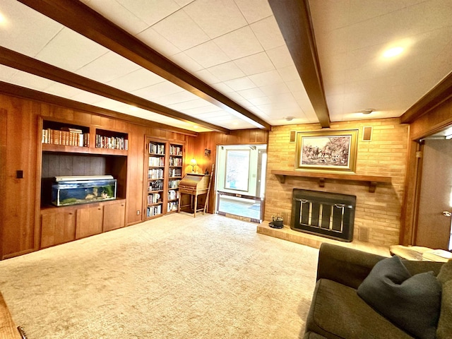 carpeted living room with beam ceiling, a brick fireplace, and wooden walls