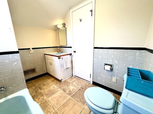 bathroom with a washtub, tile walls, vanity, a textured ceiling, and toilet