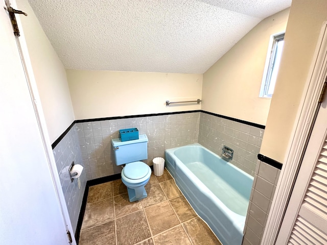 bathroom featuring lofted ceiling, tile walls, a textured ceiling, a tub to relax in, and toilet