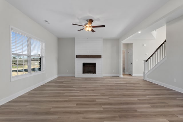 unfurnished living room featuring ceiling fan, a large fireplace, and light hardwood / wood-style floors