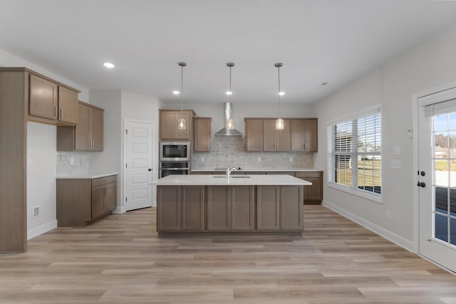 kitchen featuring built in microwave, stainless steel oven, sink, an island with sink, and decorative light fixtures