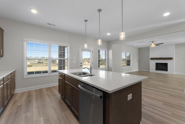 kitchen featuring stainless steel dishwasher, sink, a fireplace, hanging light fixtures, and an island with sink