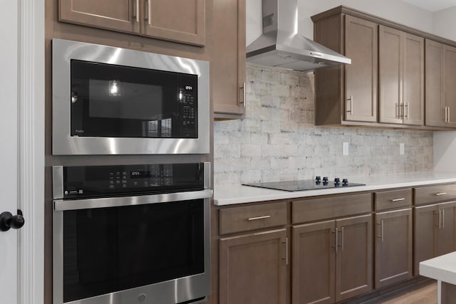 kitchen with built in microwave, stainless steel oven, wall chimney exhaust hood, backsplash, and black electric stovetop