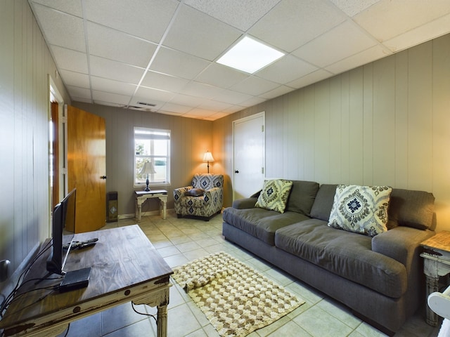 living room with a paneled ceiling, wood walls, and light tile patterned flooring