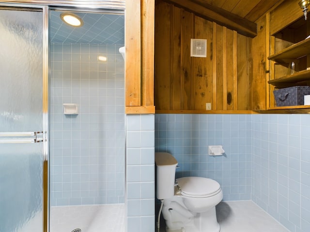 bathroom with toilet, a shower with door, and tile walls