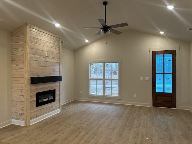 unfurnished living room featuring lofted ceiling, a glass covered fireplace, ceiling fan, wood finished floors, and baseboards