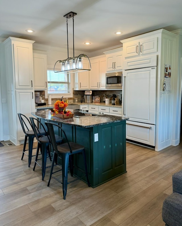 kitchen with hanging light fixtures, white cabinetry, a kitchen island, dark stone countertops, and built in appliances