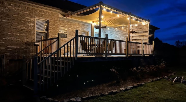 back of house at night featuring brick siding and a wooden deck