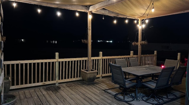 deck at night featuring outdoor dining area and a water view