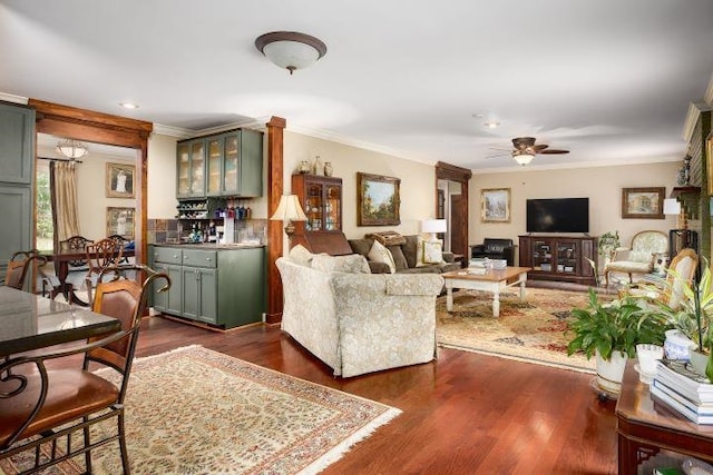  - living area with crown molding, a ceiling fan, dark wood-type flooring, and a bar