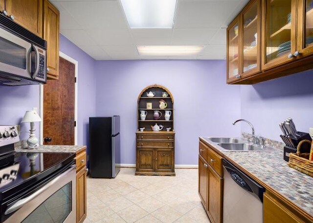  - kitchen with appliances with stainless steel finishes, a drop ceiling, brown cabinetry, glass insert cabinets, and light tile patterned floors