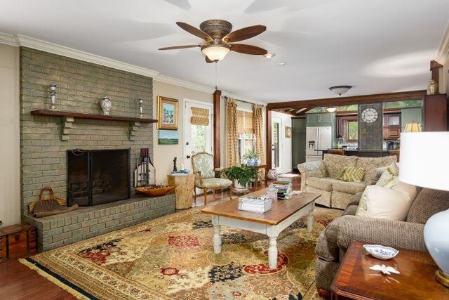  - living area with ornamental molding, ceiling fan, wood finished floors, and a fireplace