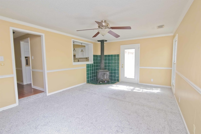 unfurnished living room with ornamental molding, carpet flooring, a textured ceiling, and a wood stove