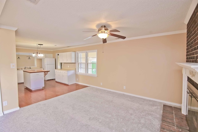 unfurnished living room with crown molding, a brick fireplace, a textured ceiling, carpet floors, and ceiling fan with notable chandelier