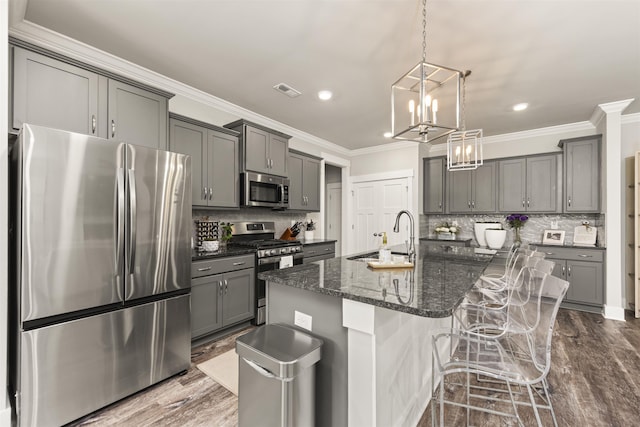  - kitchen with stainless steel appliances, gray cabinetry, an island with sink, tasteful backsplash, and crown molding
