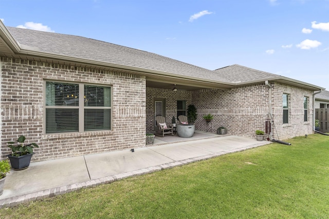  - back of house with brick siding, a patio, a yard, and roof with shingles