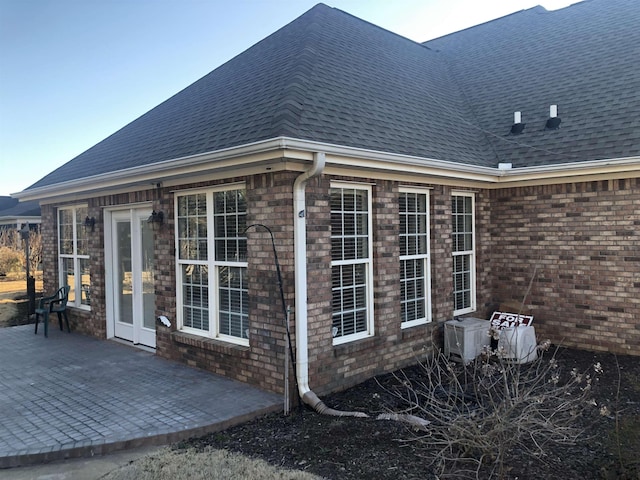 view of side of home with a patio area, brick siding, and roof with shingles