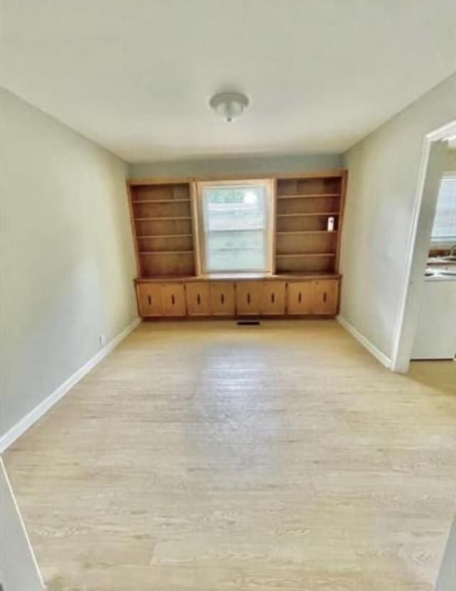 spare room featuring built in shelves, light hardwood / wood-style flooring, and plenty of natural light