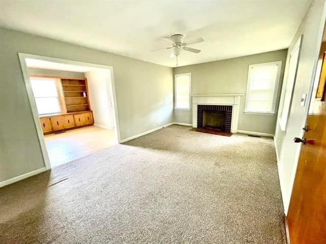 unfurnished living room featuring carpet, a wealth of natural light, a fireplace, and ceiling fan