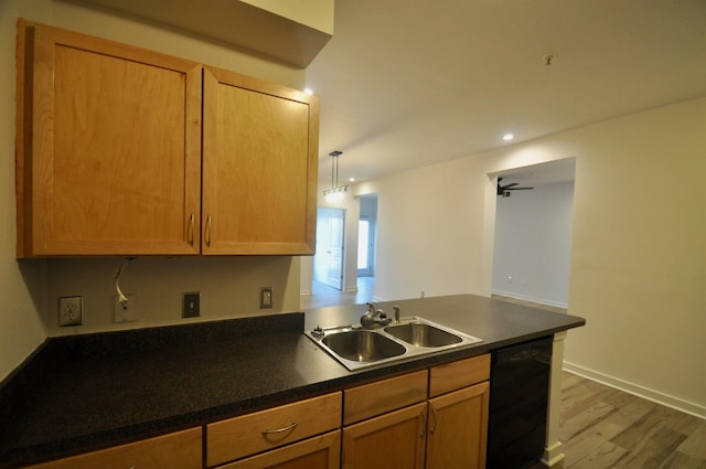 kitchen with wood finished floors, a peninsula, a sink, black dishwasher, and dark countertops