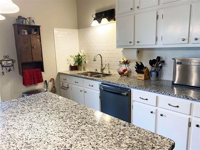  - kitchen with black dishwasher, a sink, backsplash, and white cabinets