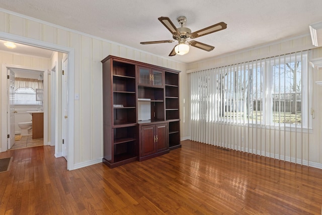 unfurnished living room with a textured ceiling, ornamental molding, dark wood finished floors, and a ceiling fan