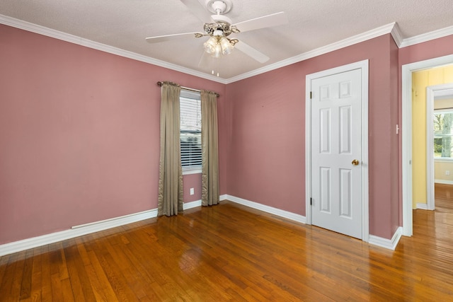 spare room with crown molding, wood-type flooring, a ceiling fan, and baseboards