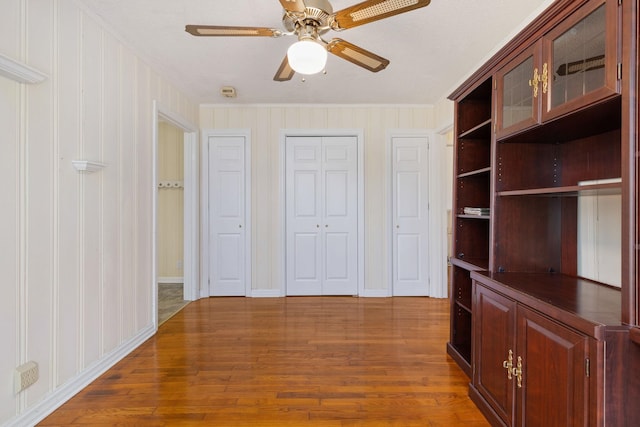 interior space with multiple closets, ceiling fan, baseboards, and wood finished floors