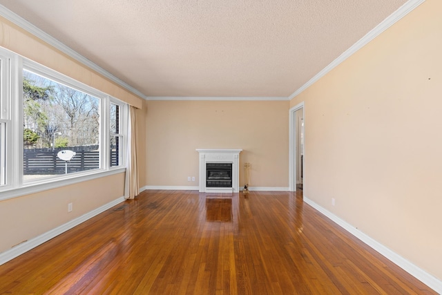 unfurnished living room with a textured ceiling, baseboards, ornamental molding, hardwood / wood-style floors, and a glass covered fireplace