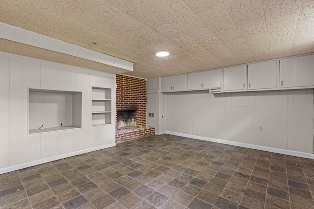 unfurnished living room featuring built in shelves, a fireplace, baseboards, wooden walls, and recessed lighting