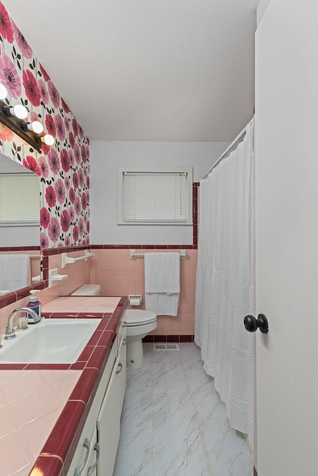 bathroom featuring tile walls, toilet, marble finish floors, a wainscoted wall, and vanity