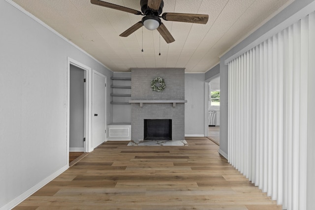 unfurnished living room featuring crown molding, a brick fireplace, a ceiling fan, light wood-style floors, and baseboards