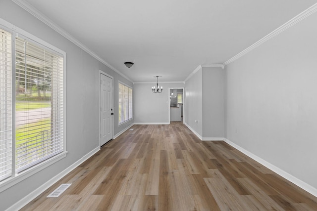 unfurnished living room with a chandelier, wood finished floors, baseboards, and ornamental molding