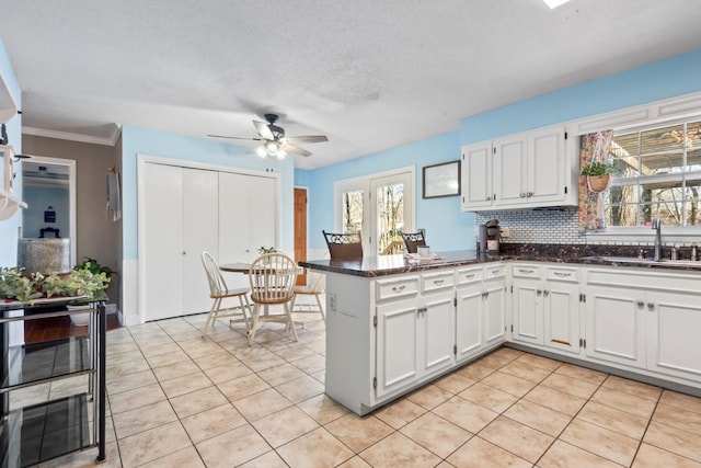 kitchen featuring sink, backsplash, kitchen peninsula, a textured ceiling, and white cabinets