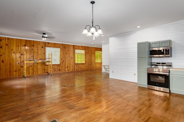 interior space featuring decorative light fixtures, wood walls, ceiling fan with notable chandelier, and appliances with stainless steel finishes