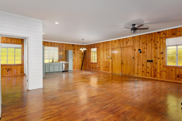 unfurnished living room with hardwood / wood-style flooring, ceiling fan with notable chandelier, a healthy amount of sunlight, and ornamental molding