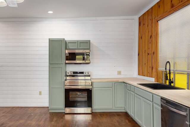 kitchen featuring green cabinets, wooden walls, sink, and stainless steel appliances