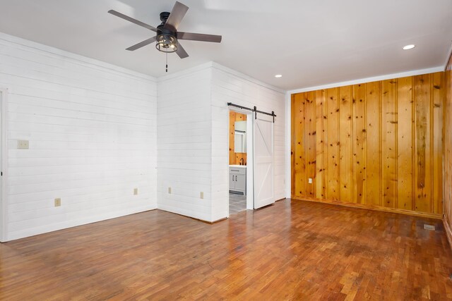 unfurnished room with ceiling fan, a barn door, and wooden walls