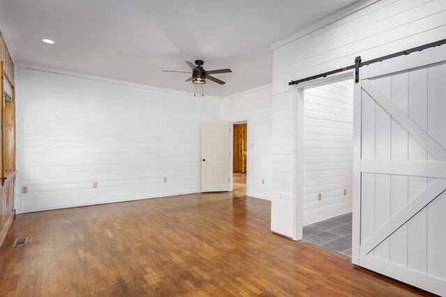 spare room with wood walls, ceiling fan, a barn door, and dark hardwood / wood-style flooring