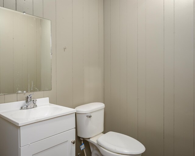 bathroom with vanity, toilet, and wooden walls