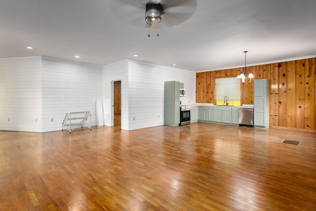 unfurnished living room with sink, ceiling fan with notable chandelier, ornamental molding, and wood walls